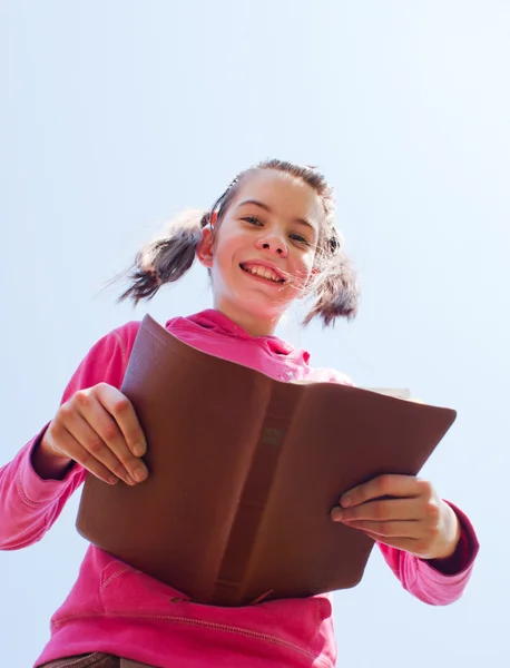 Девочка-подросток, читающая Библию против голубого неба — стоковое фото