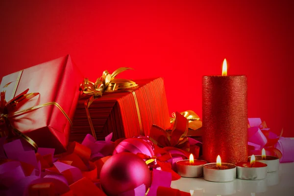 Christmas gifts and candles over red background — Stock Photo, Image