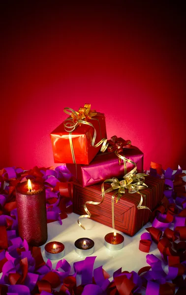 Weihnachtsgeschenke und Kerzen auf rotem Hintergrund — Stockfoto