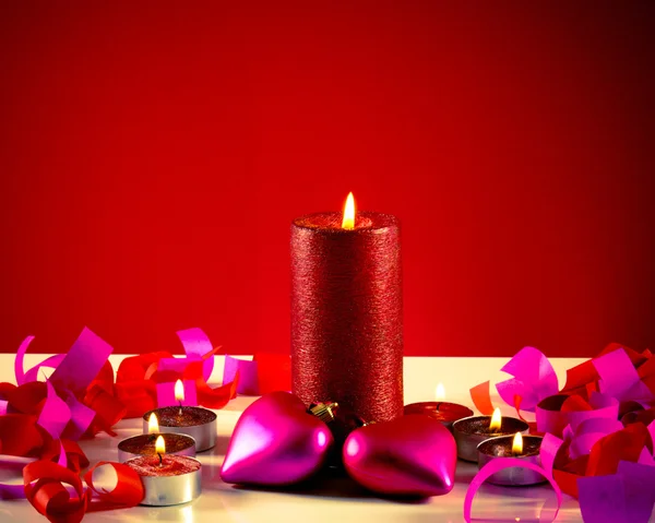 Velas ardientes con dos juguetes en forma de corazón sobre fondo rojo — Foto de Stock