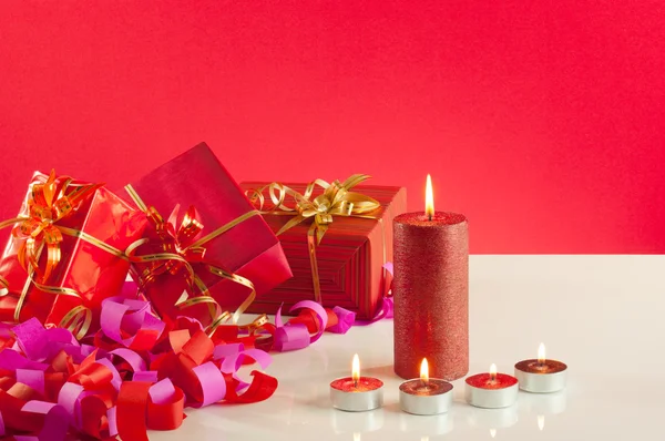クリスマスのギフトおよび赤い背景の上の蝋燭 — ストック写真