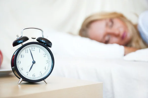 Yatak ve çalar saat uyuyan kadın — Stok fotoğraf