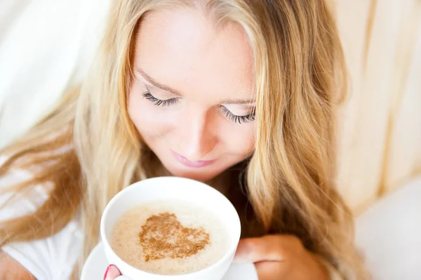 Улыбающаяся женщина пьет кофе, лежащий на кровати дома или в отеле . — стоковое фото