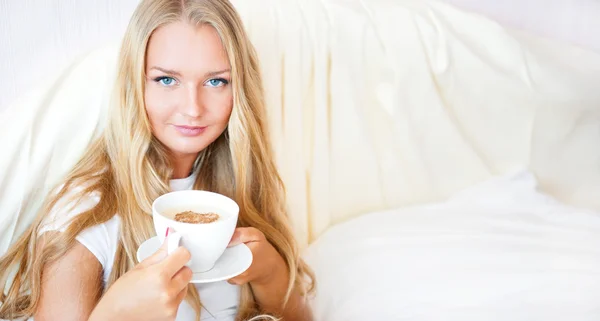 Uśmiechający się picia kawy, leżąc na łóżku w domu lub w hotelu. — Zdjęcie stockowe