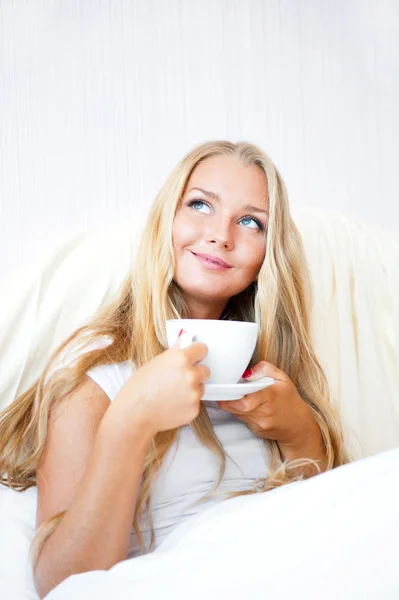 Mulher sorridente bebendo um café deitado em uma cama em casa ou hotel . — Fotografia de Stock