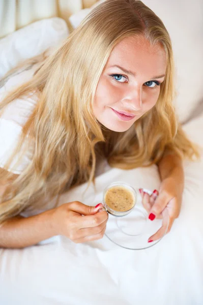 Mulher sorridente bebendo um café deitado em um sofá em casa — Fotografia de Stock