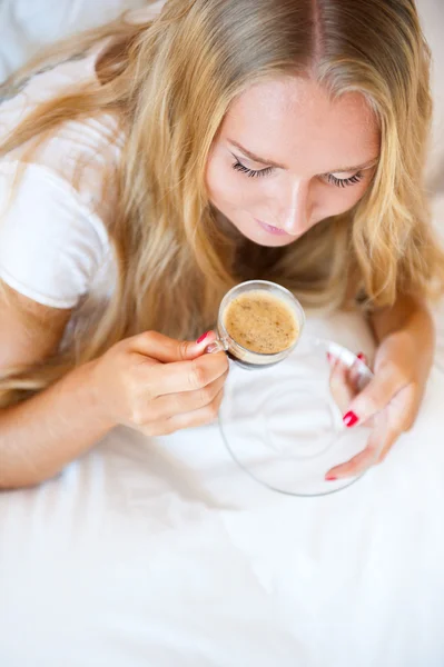 Smiling woman drinking a coffee lying on a sofa at home — Stock Photo, Image