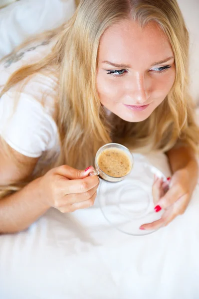 Mujer sonriente bebiendo un café tumbada en un sofá en casa — Foto de Stock