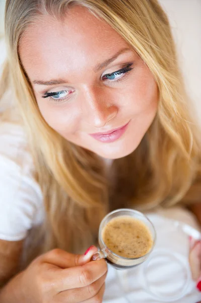 Mujer sonriente bebiendo un café tumbada en un sofá en casa —  Fotos de Stock