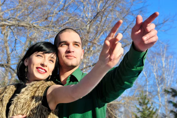 Young couple standing together in winter park, pointing and look — Stock Photo, Image
