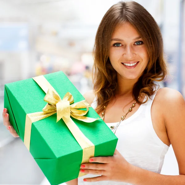 Beautiful brunette woman with a gift boxe standing inside shoppi — Stock Photo, Image