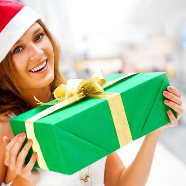 Joven mujer sonriente sosteniendo regalo de pie en el centro comercial weari — Foto de Stock