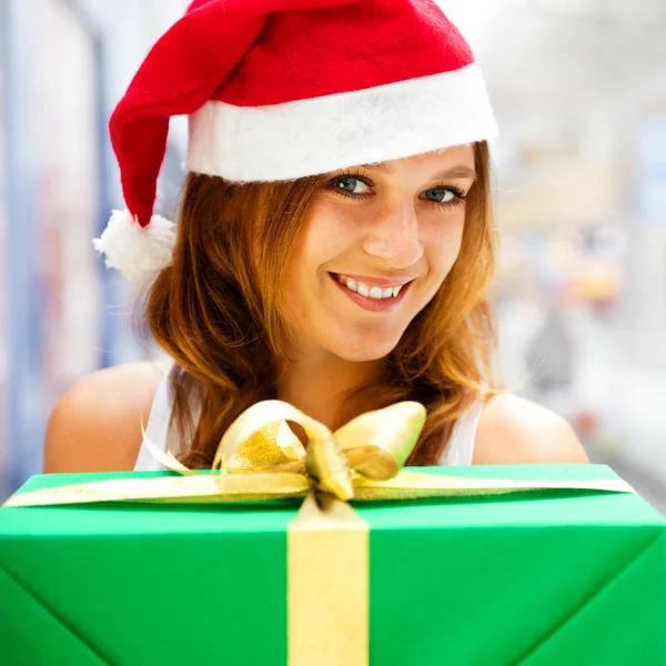 Joven mujer sonriente sosteniendo regalo de pie en el centro comercial weari — Foto de Stock
