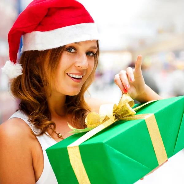 Jovem mulher sorridente segurando presente de pé no shopping shopping weari — Fotografia de Stock