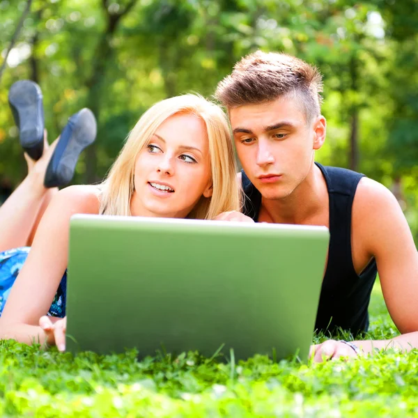 Portrait of young couple outdoor resting on green grass and usin — Stock Photo, Image