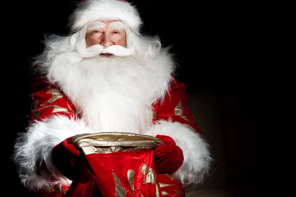 Santa sitter vid jul rum och tittar in i säcken — Stockfoto