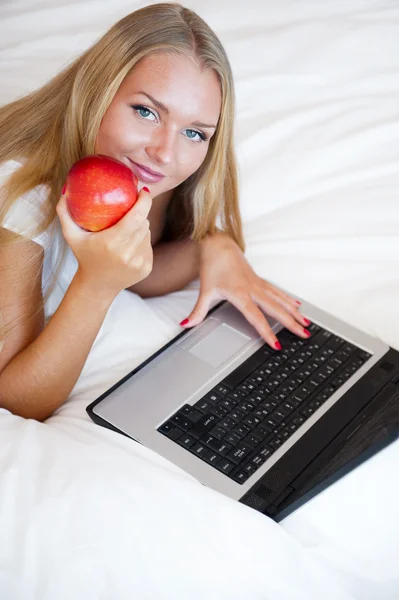 그녀의 침대에 누워 및 r를 먹는 동안 노트북을 사용 하 여 웃는 여자 — 스톡 사진
