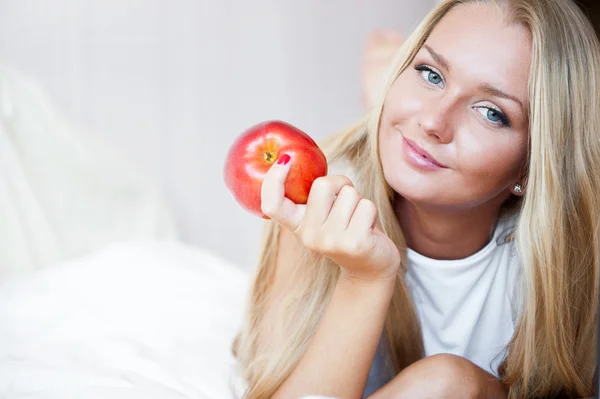 Petite femme souriante allongée sur son lit et mangeant de la pomme rouge — Photo