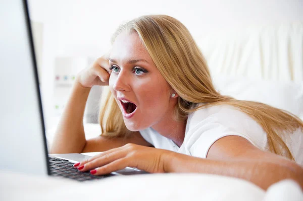 Smiling woman using a laptop while lying on her bed and playing — Stock Photo, Image