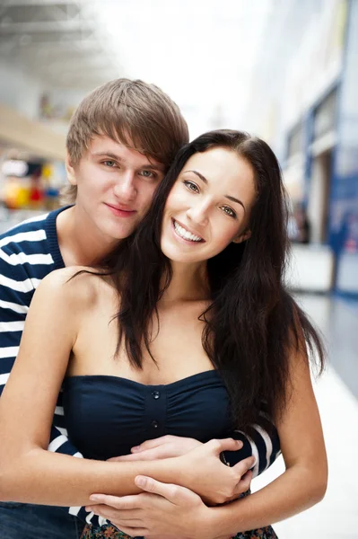 Portrait of young couple embracing at shopping mall and looking — Stock Photo, Image