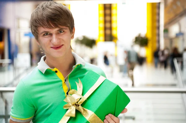 Portrait of young man inside shopping mall with gift box sitting — Stock Photo, Image