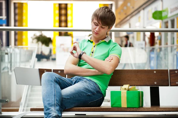 Ritratto di giovane all'interno di un centro commerciale con scatola regalo seduto — Foto Stock