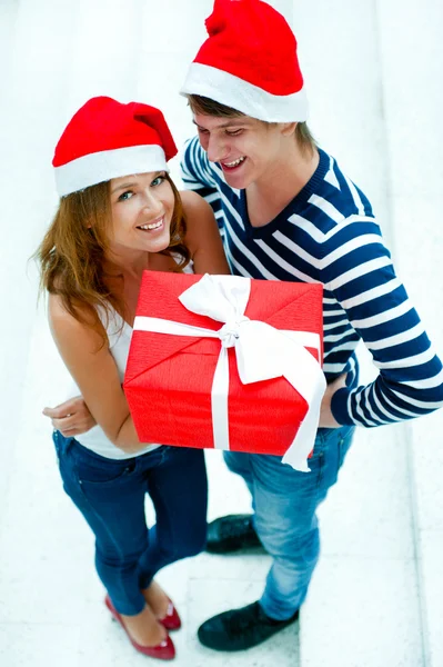 Jeune couple heureux dans chapeaux de Noël debout ensemble et holdi — Photo