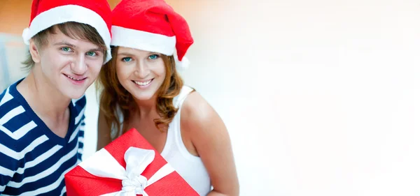 Joven pareja feliz en sombreros de Navidad de pie juntos y holdi —  Fotos de Stock