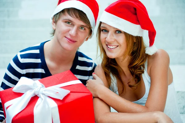 Jovem casal feliz em chapéus de Natal de pé juntos e holdi — Fotografia de Stock