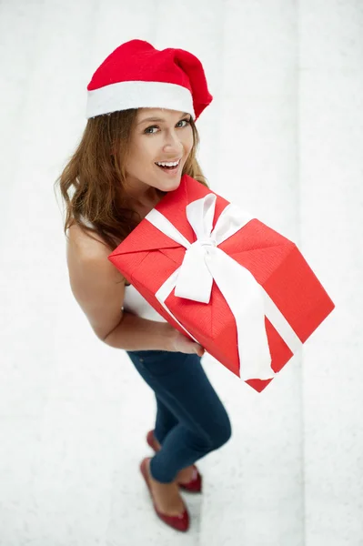 Молодая счастливая девушка в рождественской шляпе. Стоя в помещении и удерживая — стоковое фото