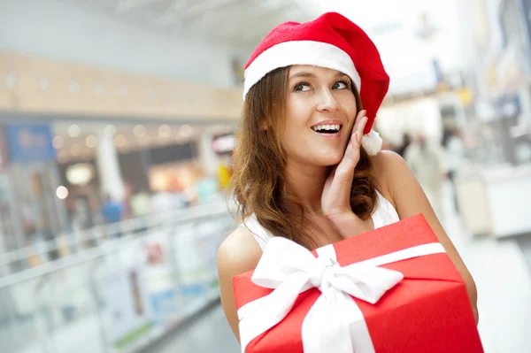 Young happy girl in Christmas hat. Standing indoors and holding — Stock Photo, Image