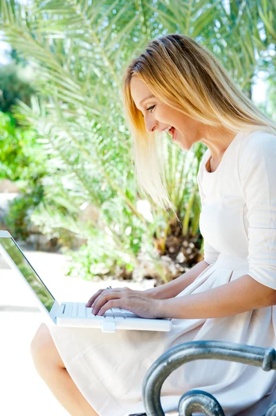 Красива жінка використовує ноутбук, сидячи розслабленим на лавці на s — стокове фото
