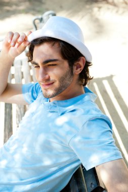 Portrait of a handsome young man sitting in the sun on bench at