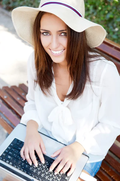 Jovem mulher elegante usando chapéu de palha e vestido branco com lapto — Fotografia de Stock