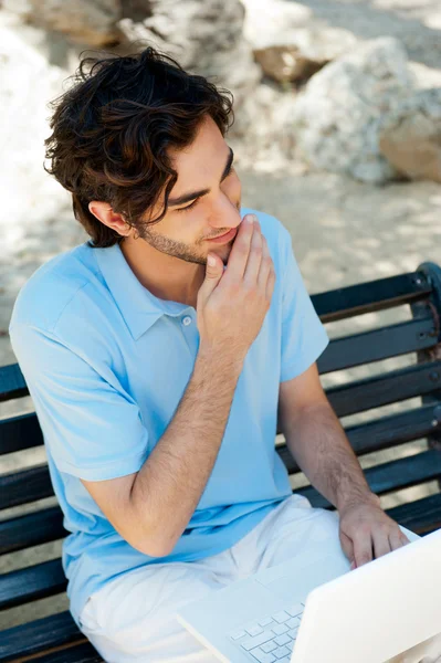 Ile dizüstü bilgisayar açık bankta oturan genç bir adam portresi — Stok fotoğraf