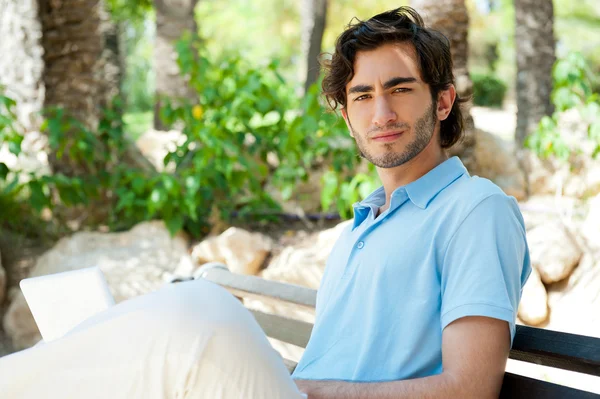 Portrait d'un jeune homme avec ordinateur portable assis en plein air sur un banc — Photo