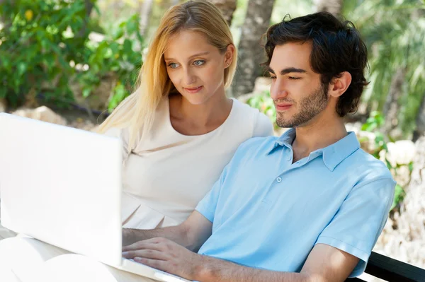 Молода пара працює на ноутбуці і посміхається, сидячи розслабленим — стокове фото