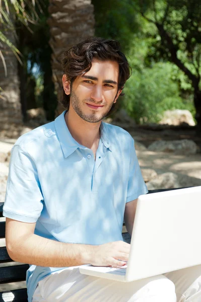 Portrait d'un jeune homme avec ordinateur portable assis en plein air sur un banc — Photo