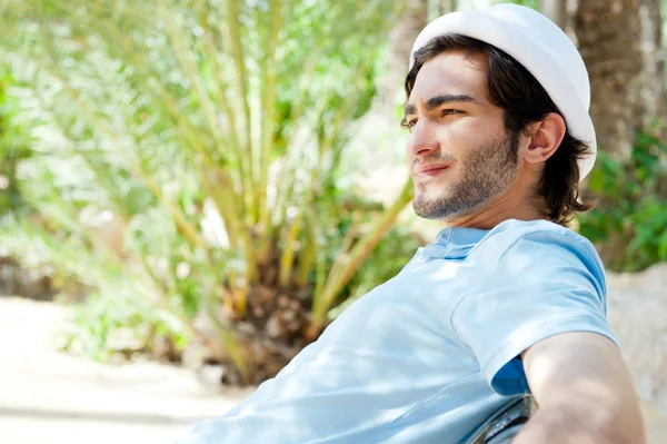 Portrait of a handsome young man sitting in the sun on bench at — Stockfoto