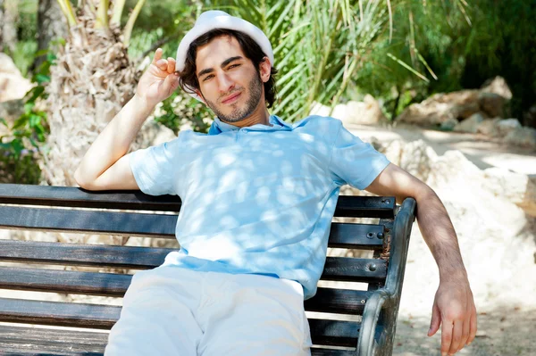 Portrait of a handsome young man sitting in the sun on bench at — Stok fotoğraf