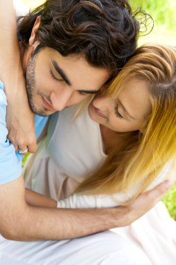 Romantic young couple sitting together in forest embracing and s clipart