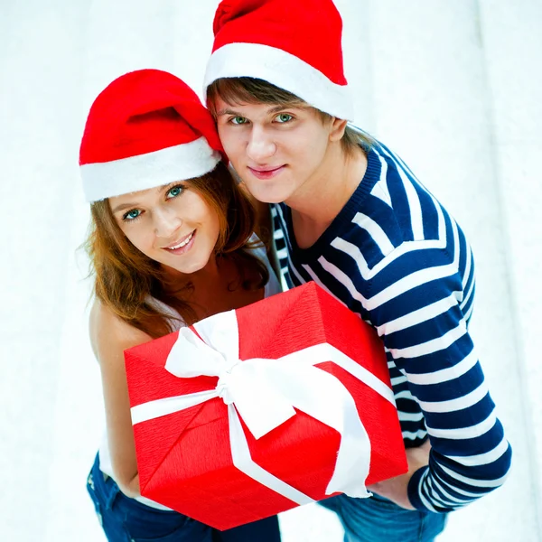 Jovem casal feliz em chapéus de Natal de pé juntos e holdi — Fotografia de Stock