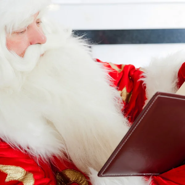 Santa sentado en el árbol de Navidad, chimenea y leyendo un boo —  Fotos de Stock