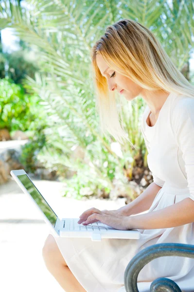Beautiful woman using laptop while sitting relaxed on bench at s — Stock Photo, Image
