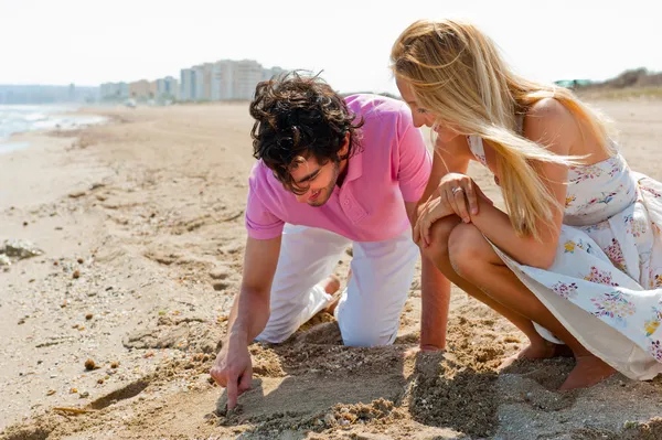 Casal apaixonado desenhando um coração na areia enquanto relaxa no bea — Fotografia de Stock
