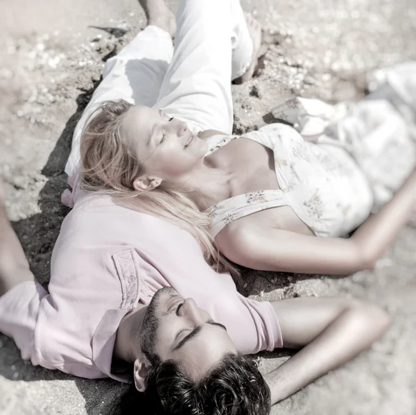 年轻夫妇放宽在海滩上的沙子上，与古人类做白日梦 — 图库照片