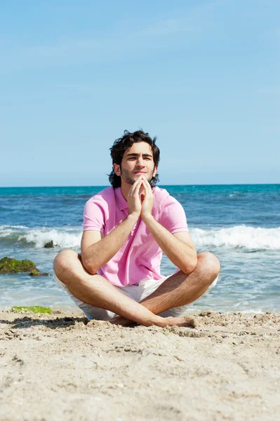 Portrait of young man sitting in lotus pose on sand on beach and — Stock Photo, Image