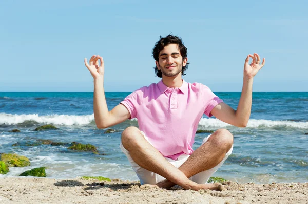 Portrait of young man sitting in lotus pose on sand on beach and — Stock Photo, Image