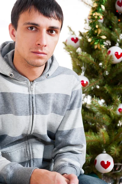 Jovem homem calmo sentado na frente da árvore de Natal — Fotografia de Stock