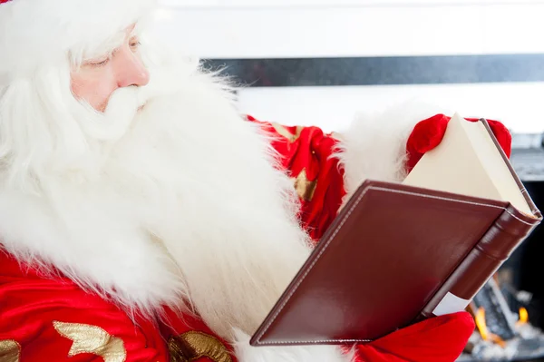 Der Weihnachtsmann sitzt am Weihnachtsbaum, am Kamin und liest ein Buh — Stockfoto